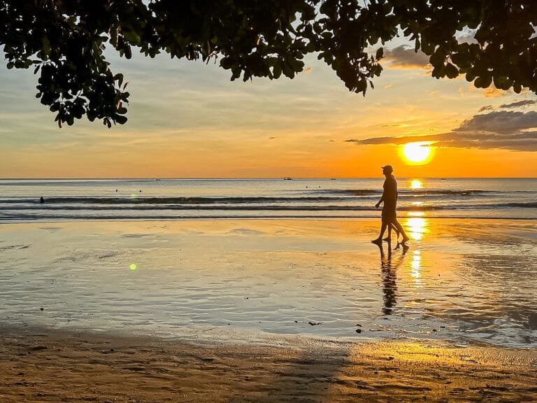 Wandelaar als silhouet op het natte strand tijdens zonsondergang
